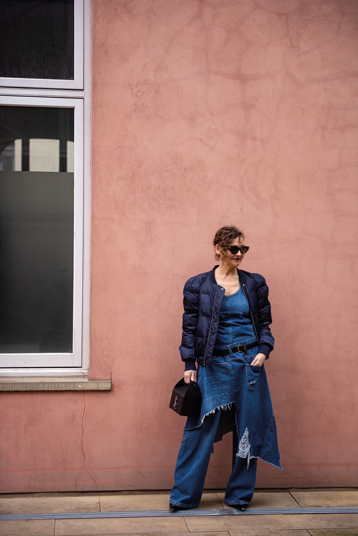 Vrouw poseert op straat in een blauwe spijkerbroek en denim blouse bij een zalmkleurige muur